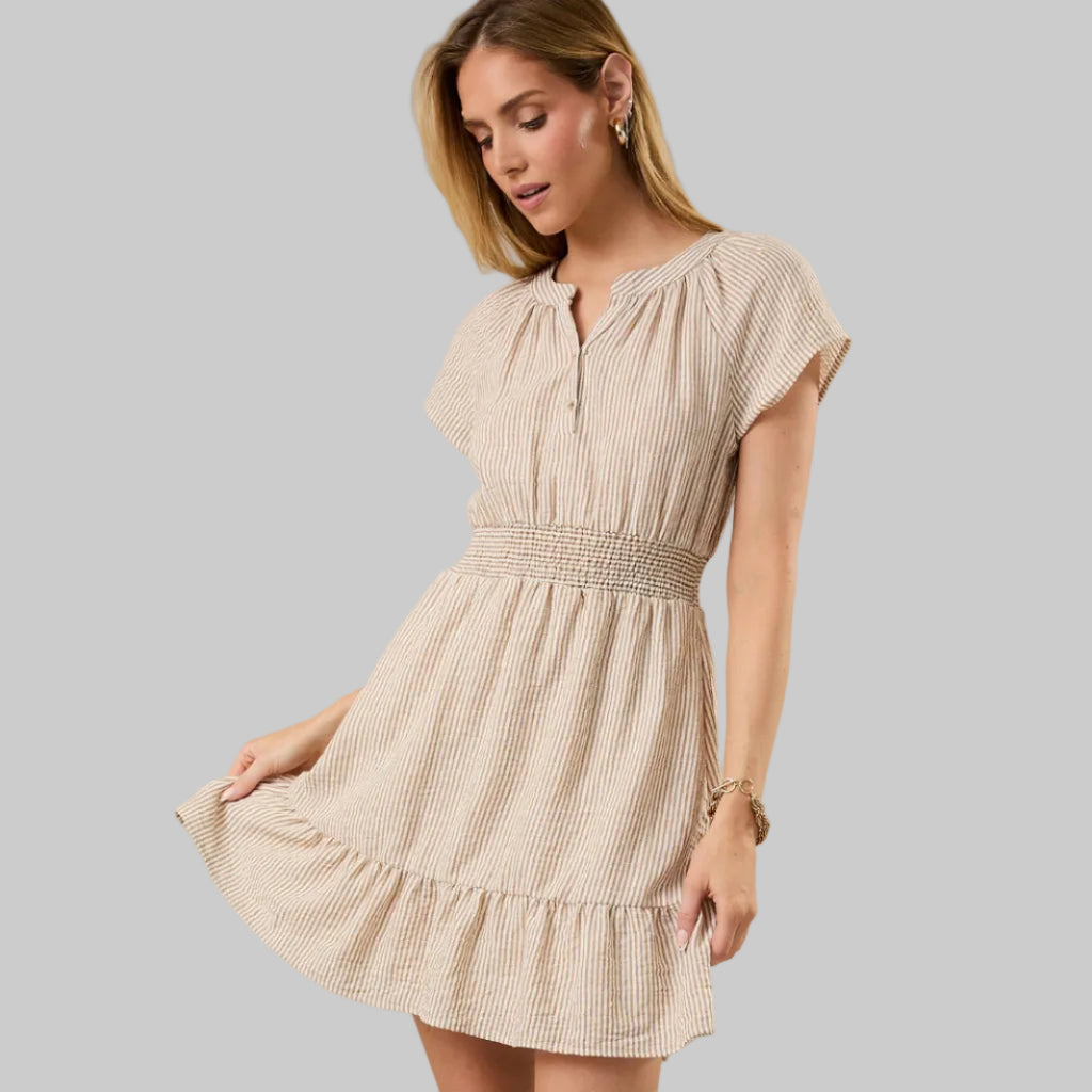 Woman wearing a beige and white striped dress against a neutral background