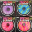Needoh donut-shaped items arranged in a 2x2 grid on a light surface. Each package shows a different bright donut design: purple with white sprinkles, blue with green swirls, pink with white sprinkles, and pink with yellow swirls.