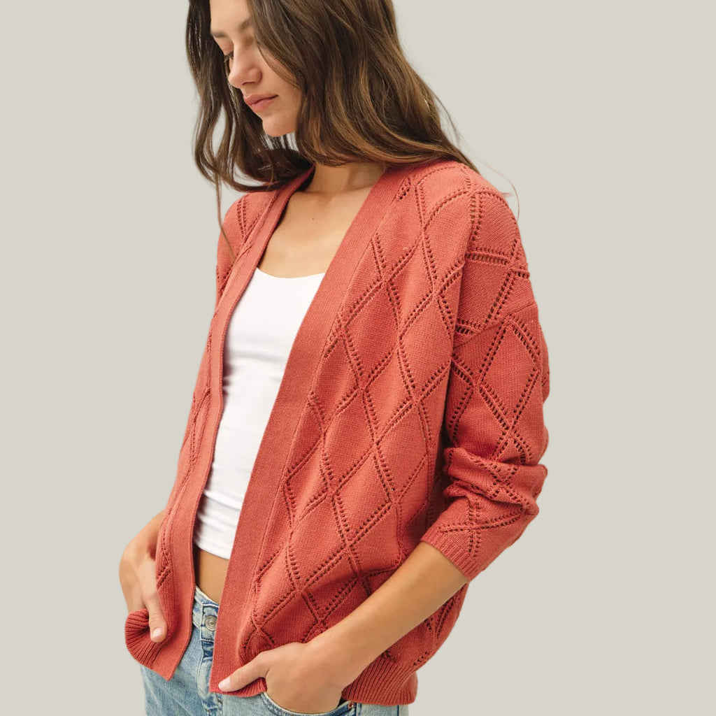 Woman wearing a pink quilted cardigan over a white shirt and blue jeans on a plain background