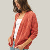 Woman wearing a pink quilted cardigan over a white shirt and blue jeans on a plain background