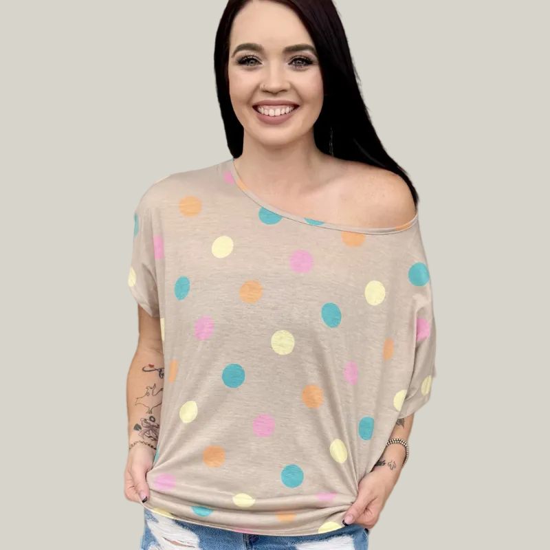 Woman wearing a beige off-shoulder top with colorful polka dots against a wooden background