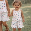 Two young girls wearing matching white dresses with colorful polka dots, standing on grass.
