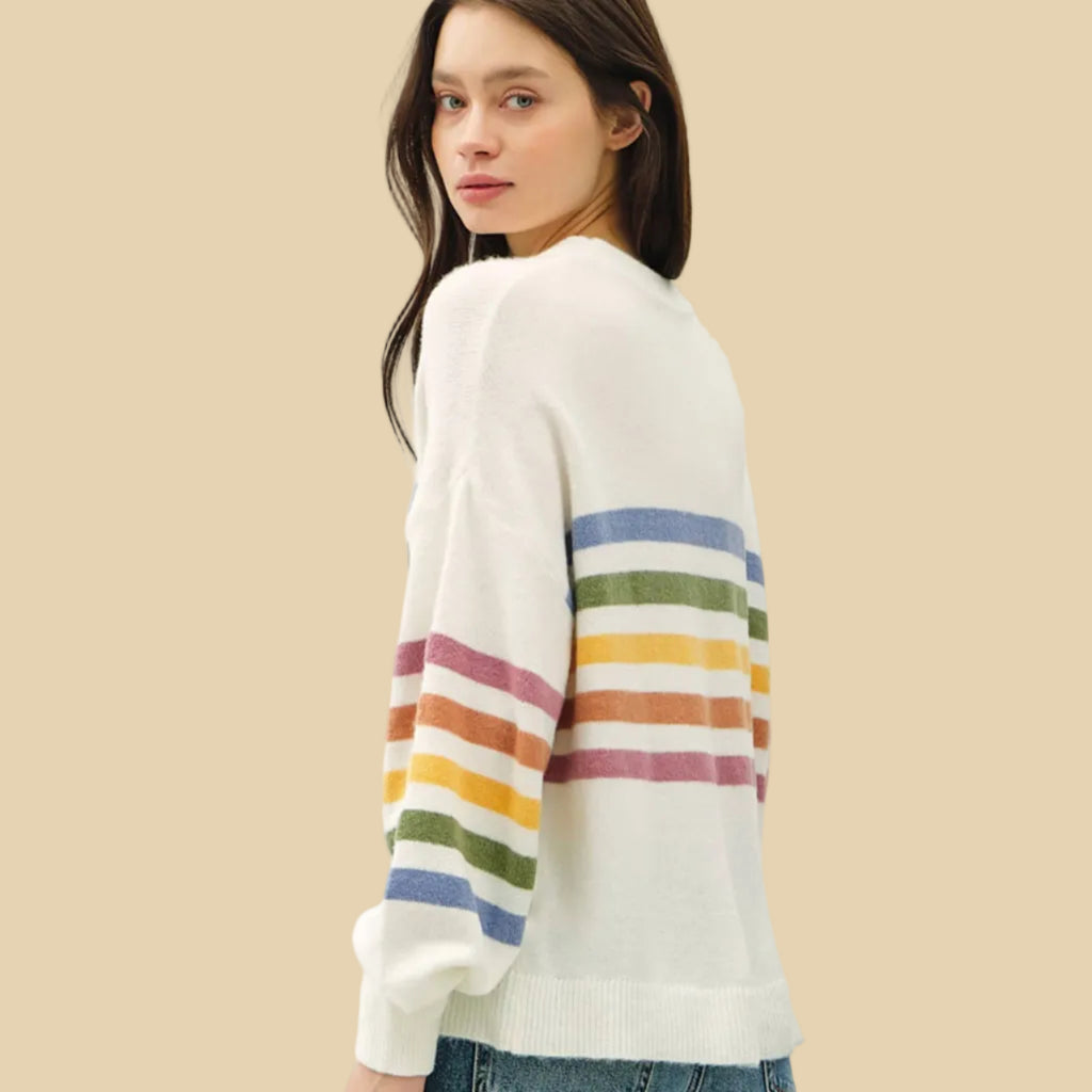 Woman wearing a white sweater with colorful stripes on a plain background