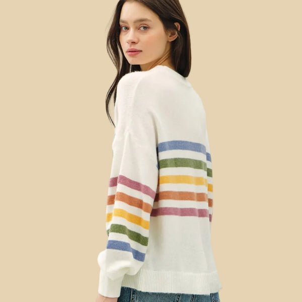 Woman wearing a white sweater with colorful stripes on a plain background