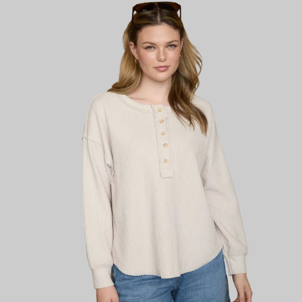Woman wearing a beige blouse with buttons and blue jeans against a neutral background