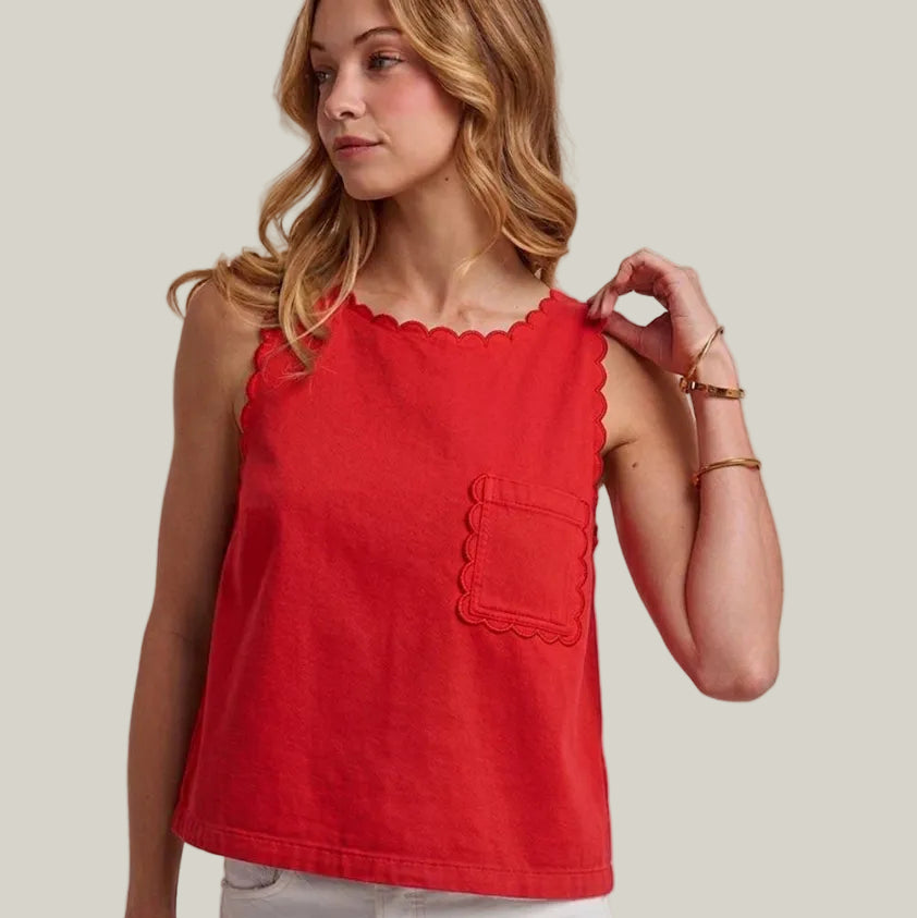Woman wearing a red sleeveless top with a scalloped neckline and pocket on a plain background