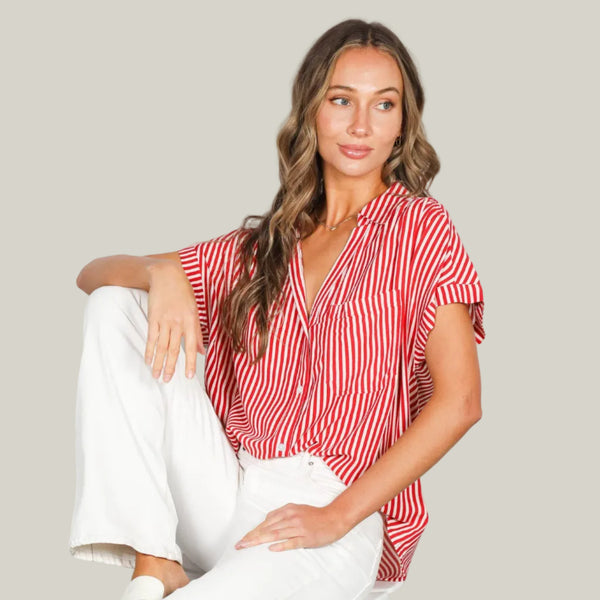Woman wearing a red and white striped top and white pants sitting on a chair against a white background