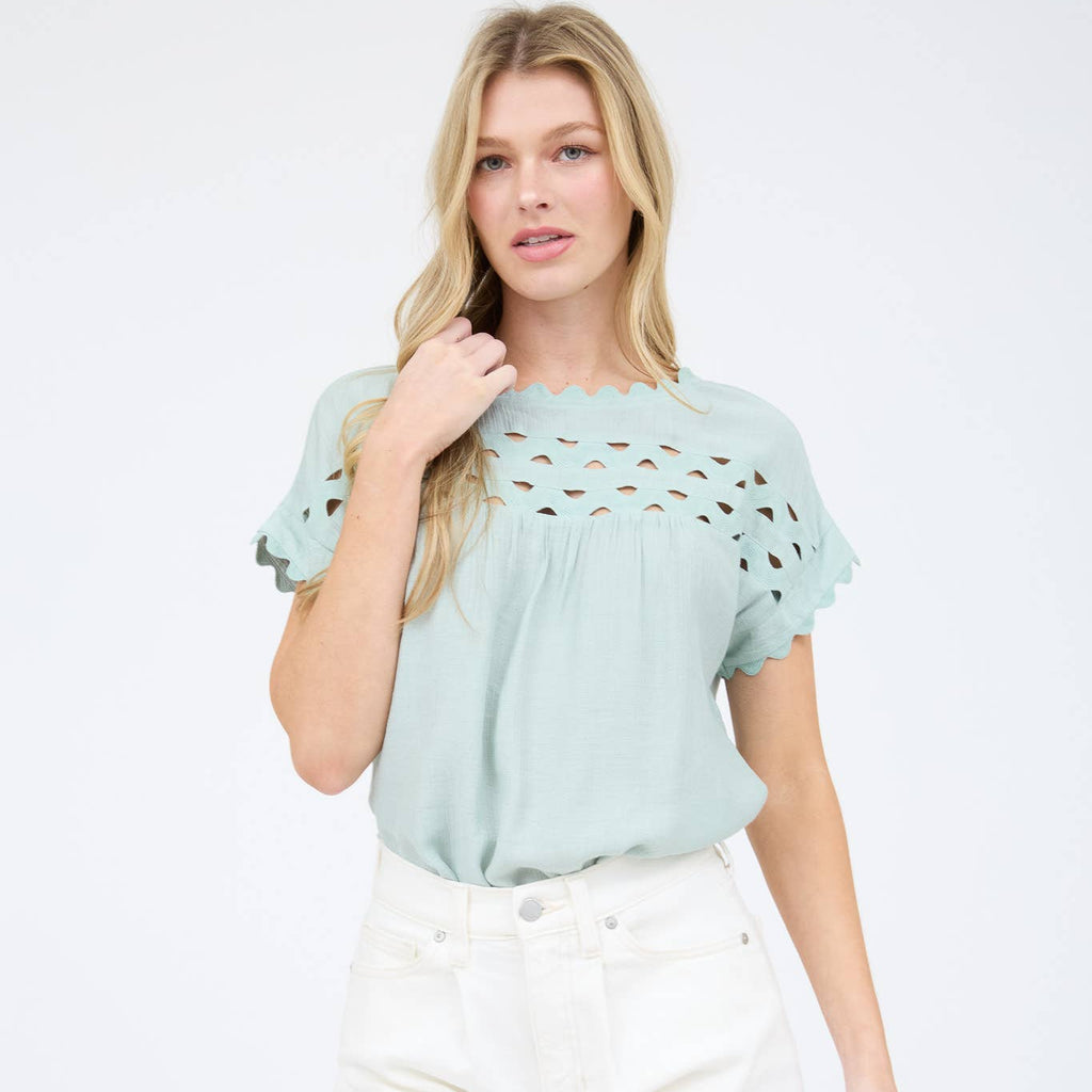 Woman wearing a light blue top with cut-out details and white shorts on a white background