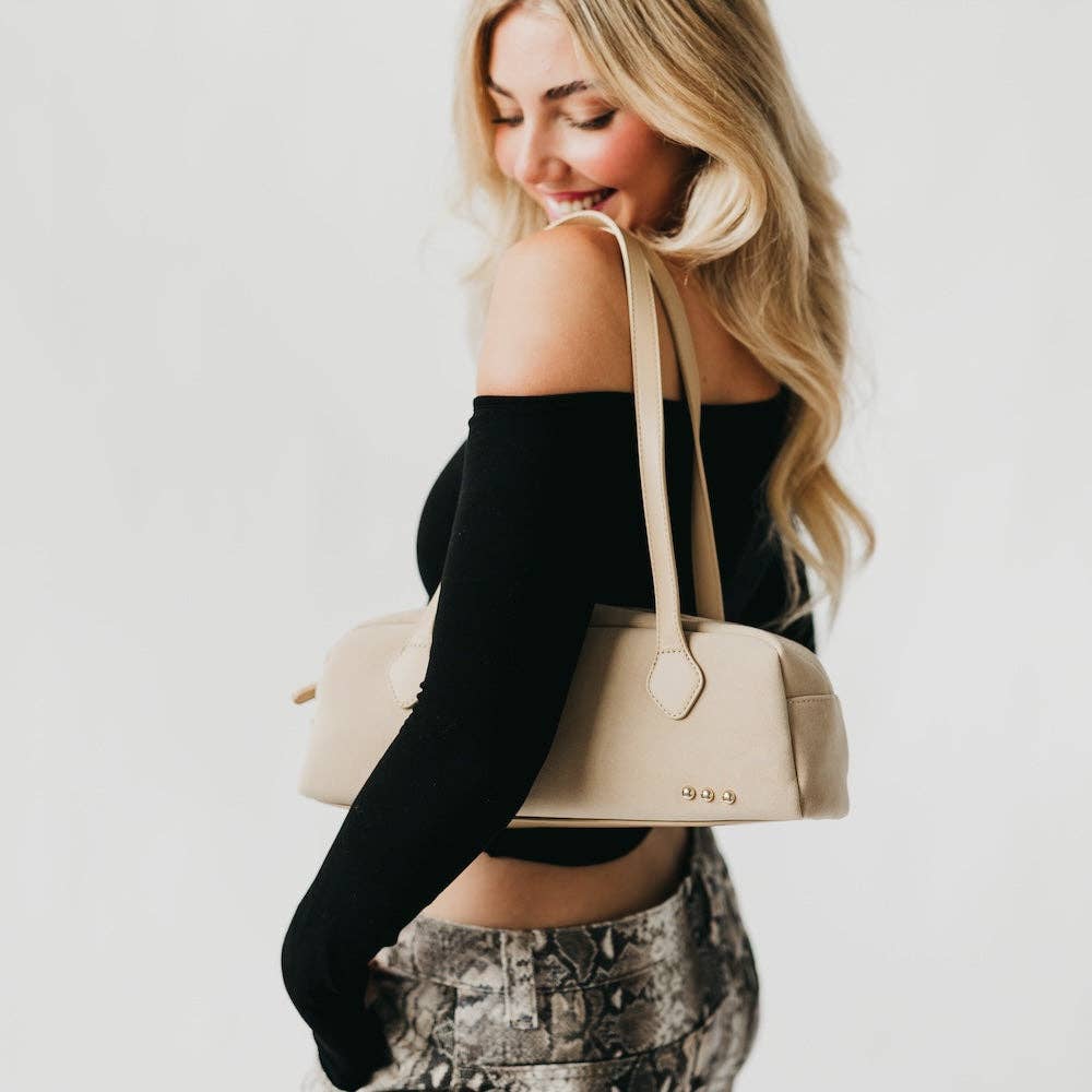 Woman holding a beige handbag against a plain background