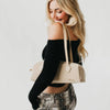 Woman holding a beige handbag against a plain background