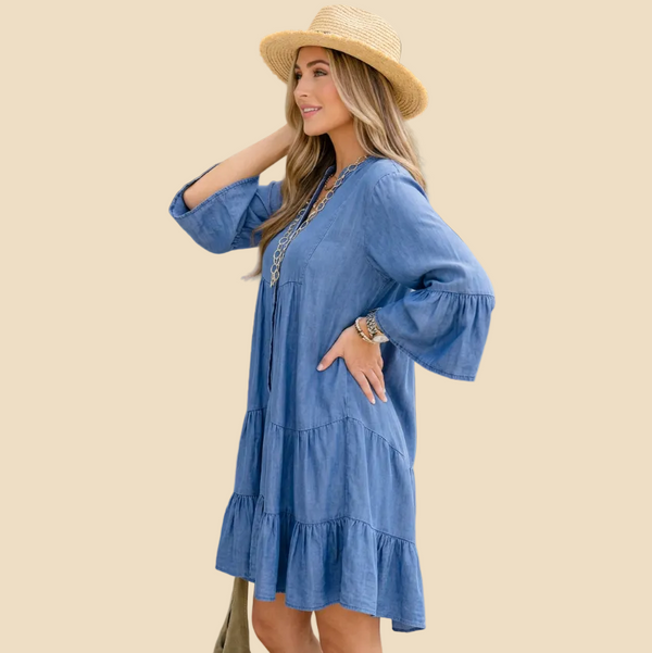 A woman wearing a blue tiered bohemian-style dress with bell sleeves and a straw hat