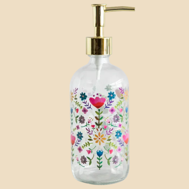 Glass soap dispenser with floral design and gold pump on a white background