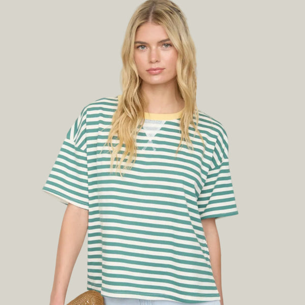 Woman wearing a green and white striped shirt with denim shorts, holding a straw hat.