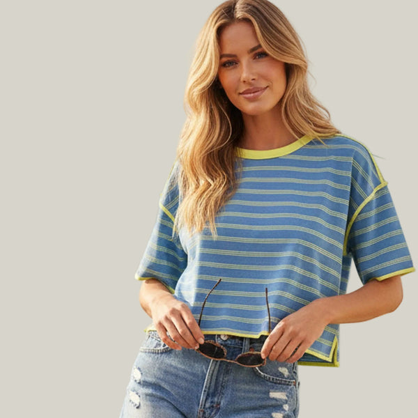Woman wearing a blue and yellow striped shirt and denim shorts standing outdoors with a scenic background.
