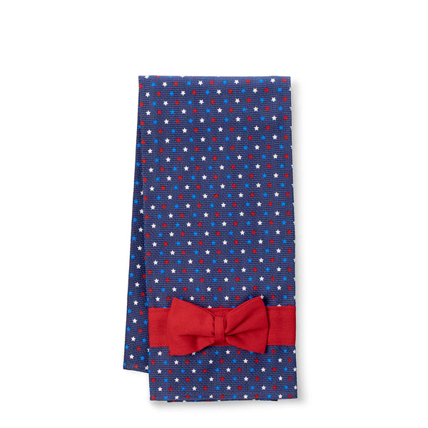Red bow tie on a folded blue polka dot fabric with white stars on a white background