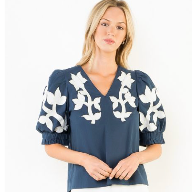 Woman wearing a navy blouse with white floral patterns on a white background