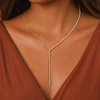 A close-up of a model wearing a delicate gold Y-necklace adorned with small clear stones, paired with a rust-brown V-neck top.