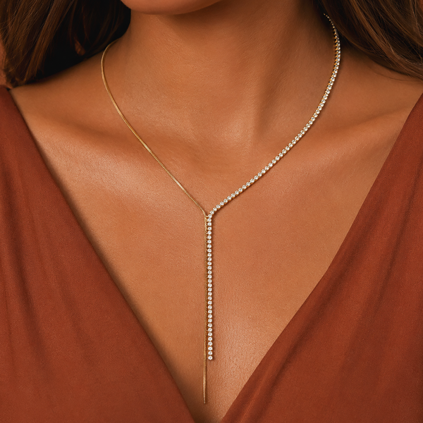 A close-up of a model wearing a delicate gold Y-necklace adorned with small clear stones, paired with a rust-brown V-neck top.