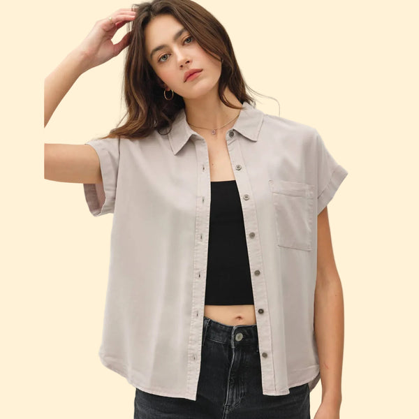 Woman wearing a light gray button-up shirt over a black top on a beige background