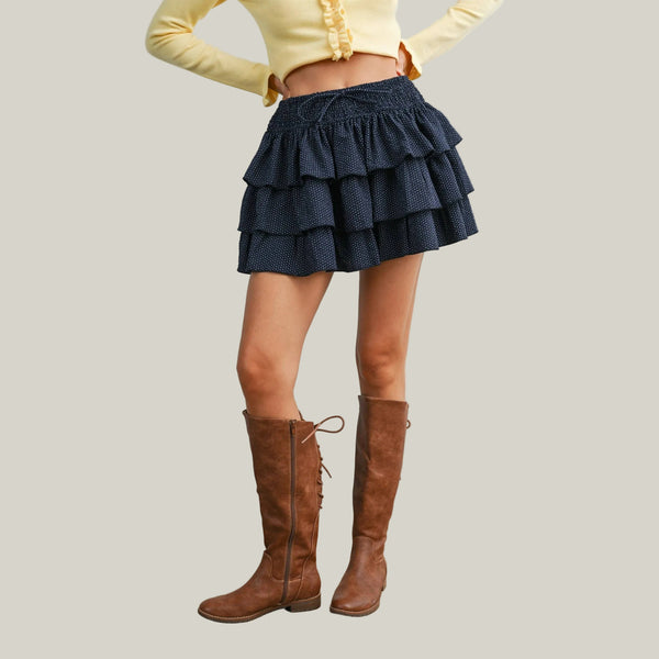 Person wearing a navy ruffled skirt and brown knee-high boots on a plain background