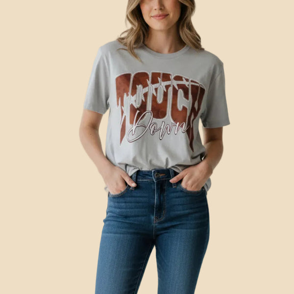 A light gray crewneck sweatshirt featuring a large graphic on the front that reads 'TOUCH Down' in brown and white, laid flat on a speckled granite countertop.