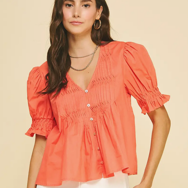 Woman wearing a coral blouse with puff sleeves on a beige background