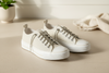 Pair of white sneakers on a light wooden floor with a neutral background