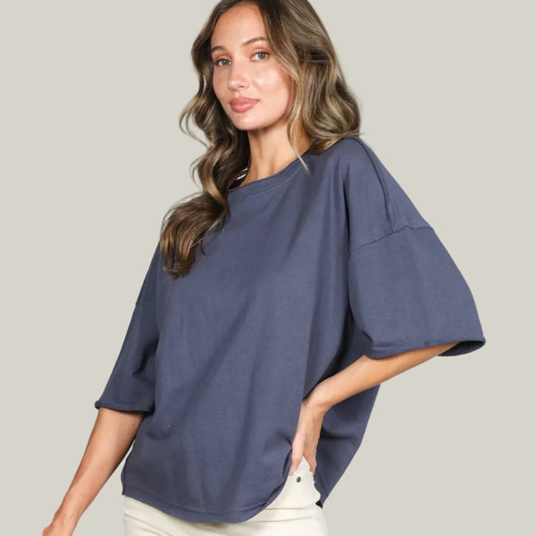 Woman wearing a blue oversized top with white pants against a white background