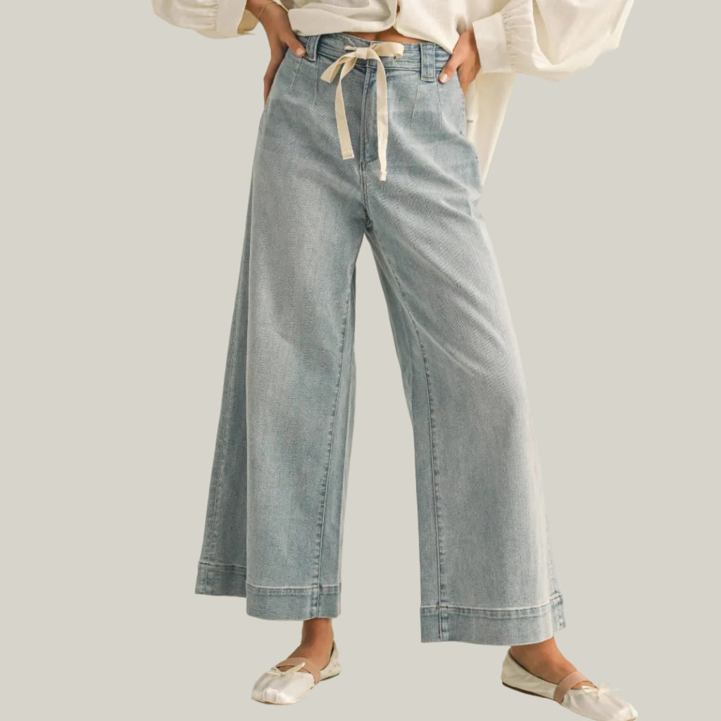 Person wearing light blue denim pants with a white shirt on a beige background