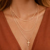 Gold necklace with a cross pendant on a person wearing a rust-colored top.