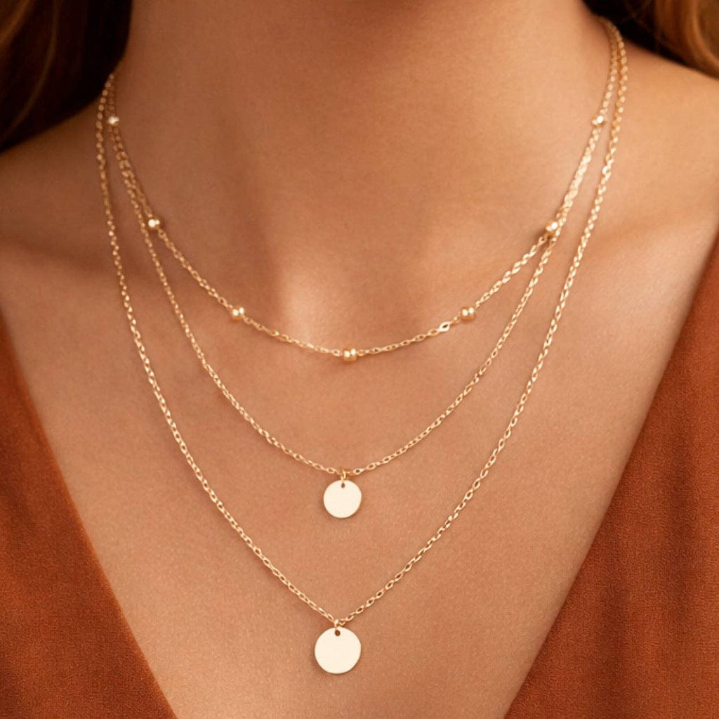 Gold necklaces with round pendants on a person wearing a rust-colored top.