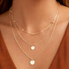 Gold necklaces with round pendants on a person wearing a rust-colored top.