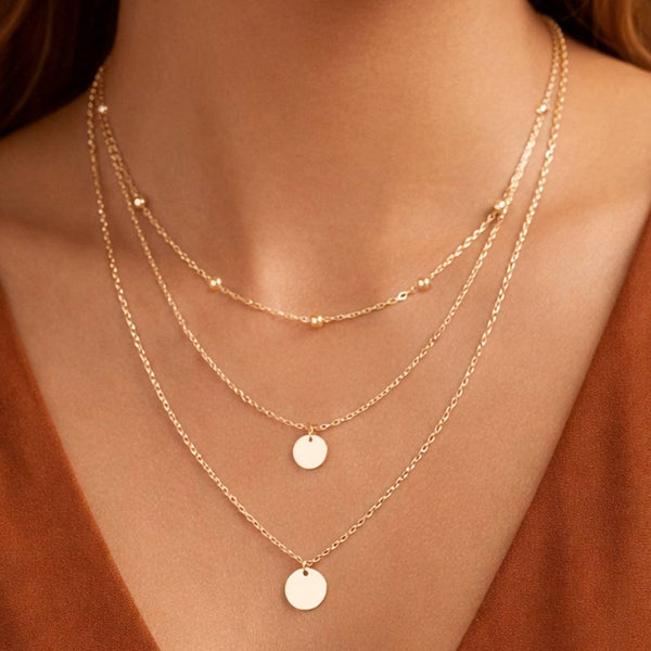 Gold necklaces with round pendants on a person wearing a rust-colored top.