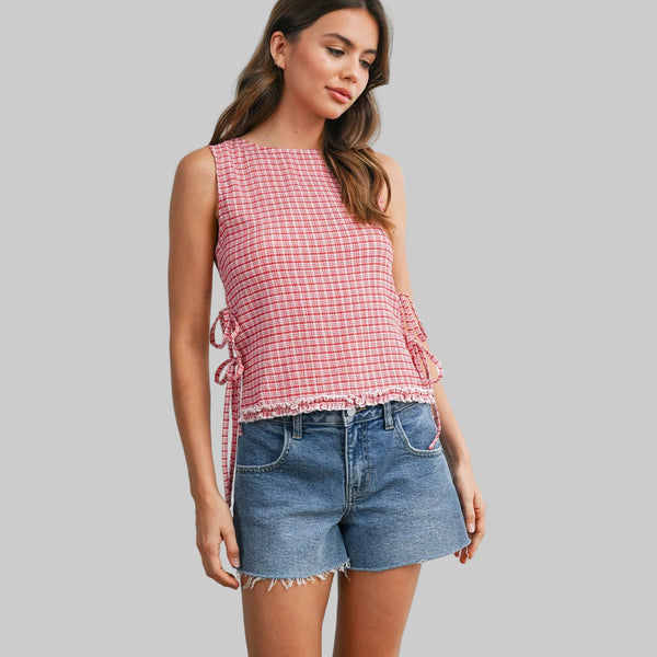 Woman wearing a red and white checkered sleeveless top and denim shorts on a light gray background