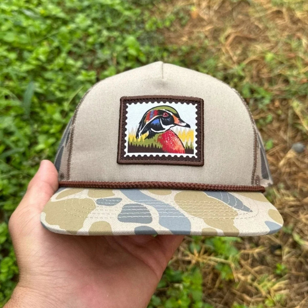 Beige cap with a colorful patch held by a hand against a grassy background
