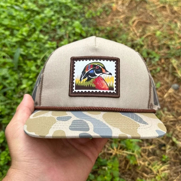 Beige cap with a colorful patch held by a hand against a grassy background