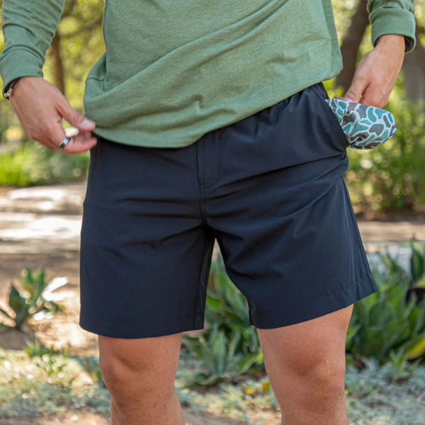 A person wearing a green top and navy Burlebo everyday shorts with a zipper and rubber buttons on the waistband.