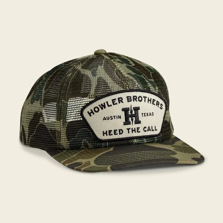 Camouflage trucker hat with 'Howler Brothers' logo on a beige background
