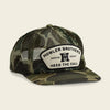 Camouflage trucker hat with 'Howler Brothers' logo on a beige background