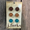 Pair of earrings on a 'j.forks Designs' card against a wooden background